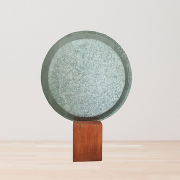 Handcrafted freestanding circular glass sculpture with crushed recycled glass fill and solid timber base – white wall and timber floor setting – modern glass art Australia