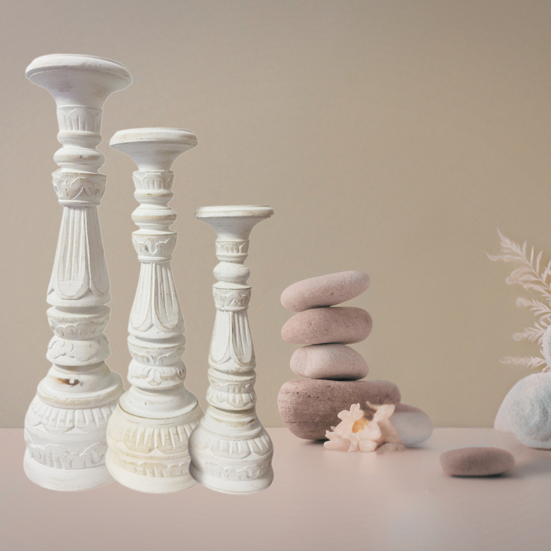 Set of white decorative candle holders with stacked stones and a shell on a neutral background