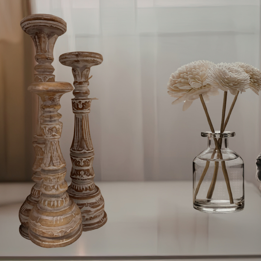 Decorative wooden candlesticks and a clear glass vase with flowers on a white surface.