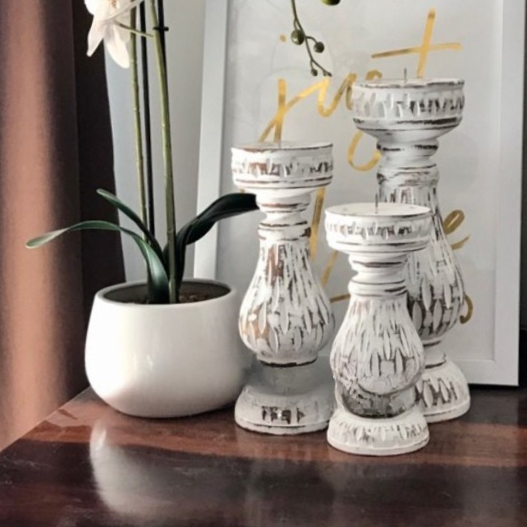 Three graduated pillar stands in distressed white styled on a dark timber console beside a white orchid plant and framed wall art