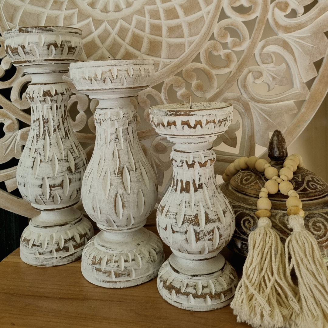 Three graduated pillar stands in distressed white styled with natural timber bead garland and tassel against a carved decorative wall panel