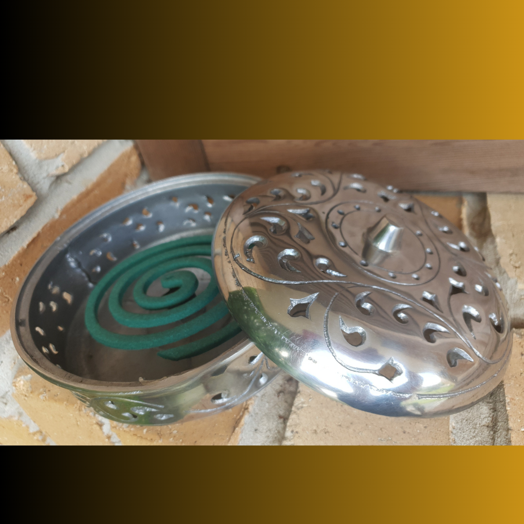 Metallic incense holder with green incense coils on a textured surface