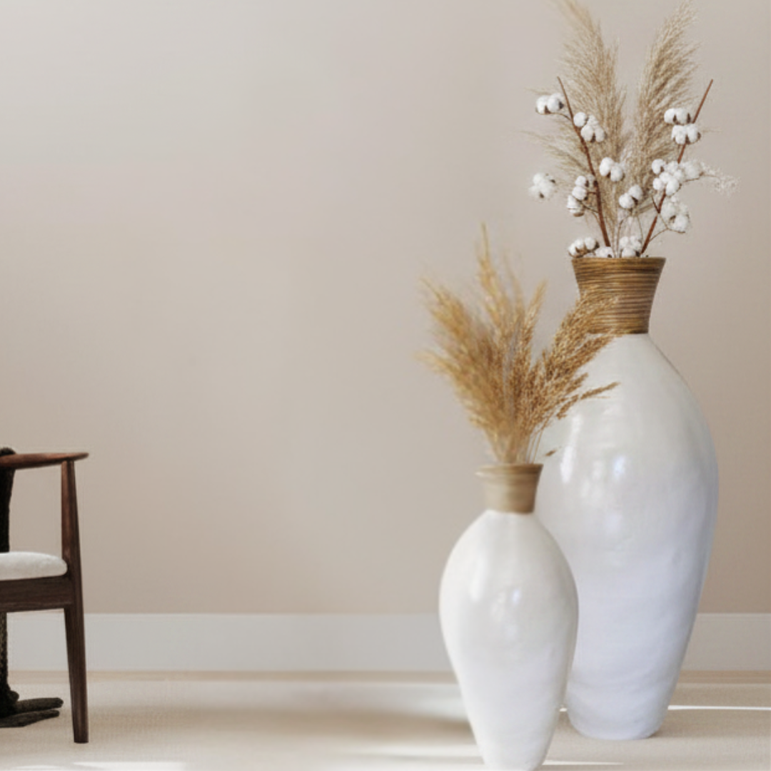 Two white vases with dried plants against a beige wall.