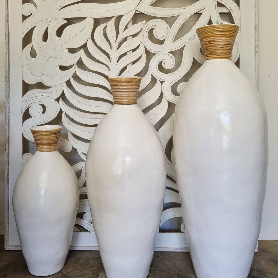 Three white vases with brown tops against a decorative wall.
