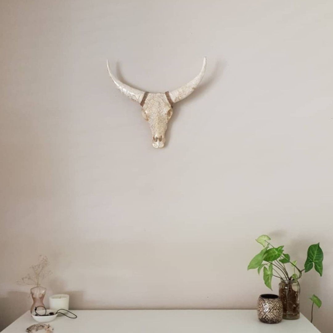 Vintage white gold wash bull skull wall art with long curved horns mounted on a neutral wall above a white console table styled with green plants and decorative vases — boho home décor by Azure Decor