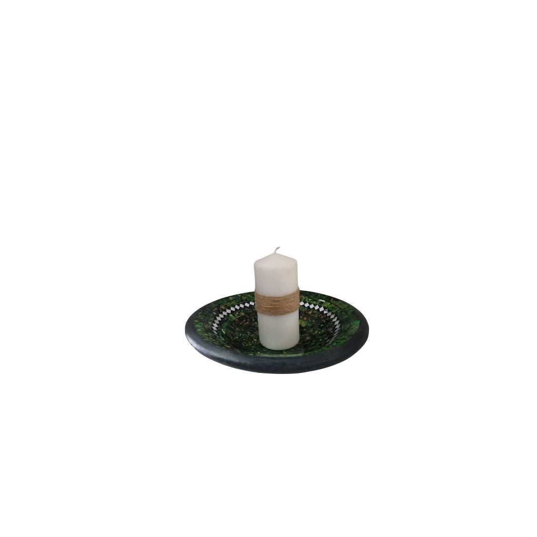 White candle on a decorative green holder with woven design on a white background