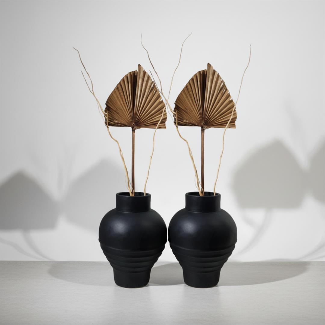 Pair of matte black globe-shaped ribbed terracotta vases styled with dried palm fan leaves on a white surface