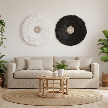 White and Black handcrafted JUJU Hat Large Designs Collection with cowrie shell centres, styled as boho feather wall art above a linen sofa in a coastal living room with rattan furniture and indoor plants