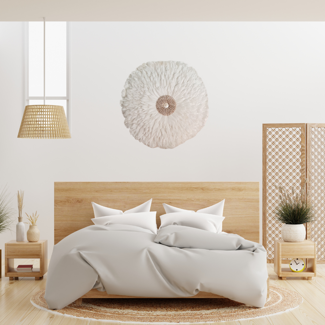 Large white handcrafted JUJU Hat with cowrie shell centre displayed as boho feather wall art above a bed in a bright Scandinavian-boho bedroom with rattan pendant light and natural timber furniture