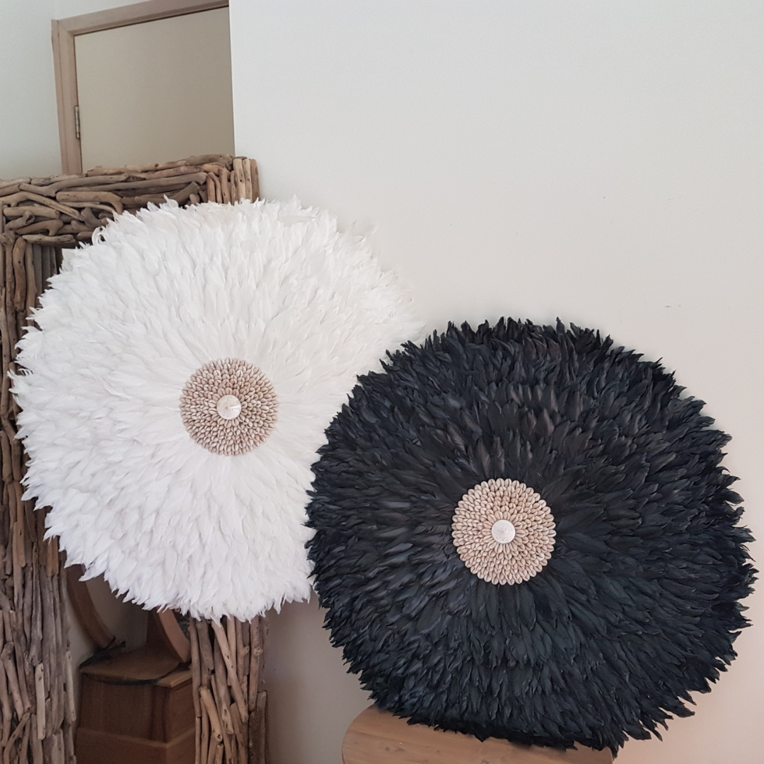 Handcrafted JUJU Hat Large Designs Collection in White and Black with cowrie shell centres, boho feather wall art, styled against driftwood furniture