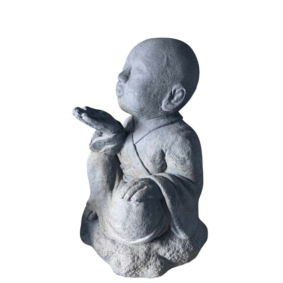 A gray stone-look figurine of a seated child monk or robed child, shown in side profile against a plain white background.