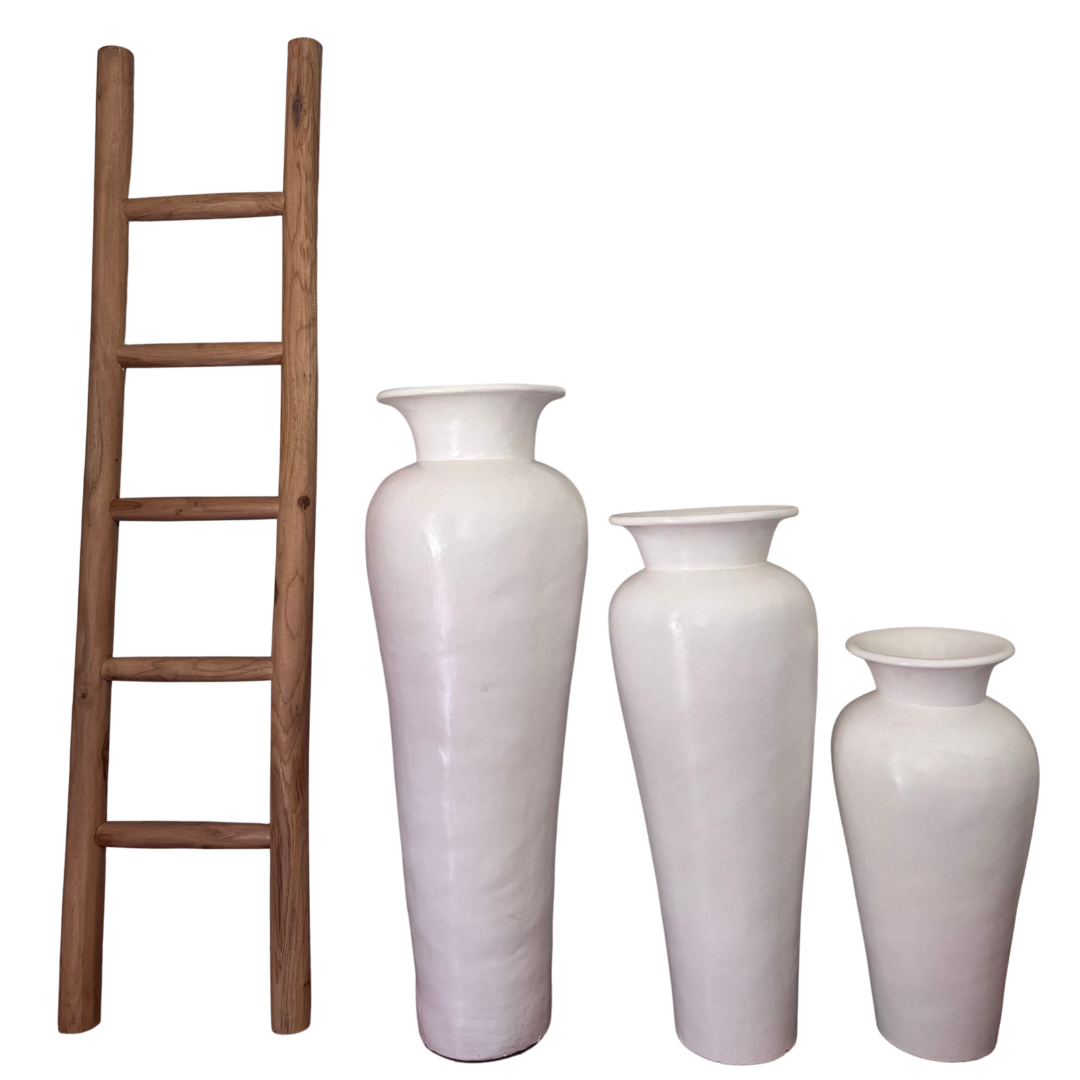 Set of three white vases of different sizes next to a wooden ladder on a white background