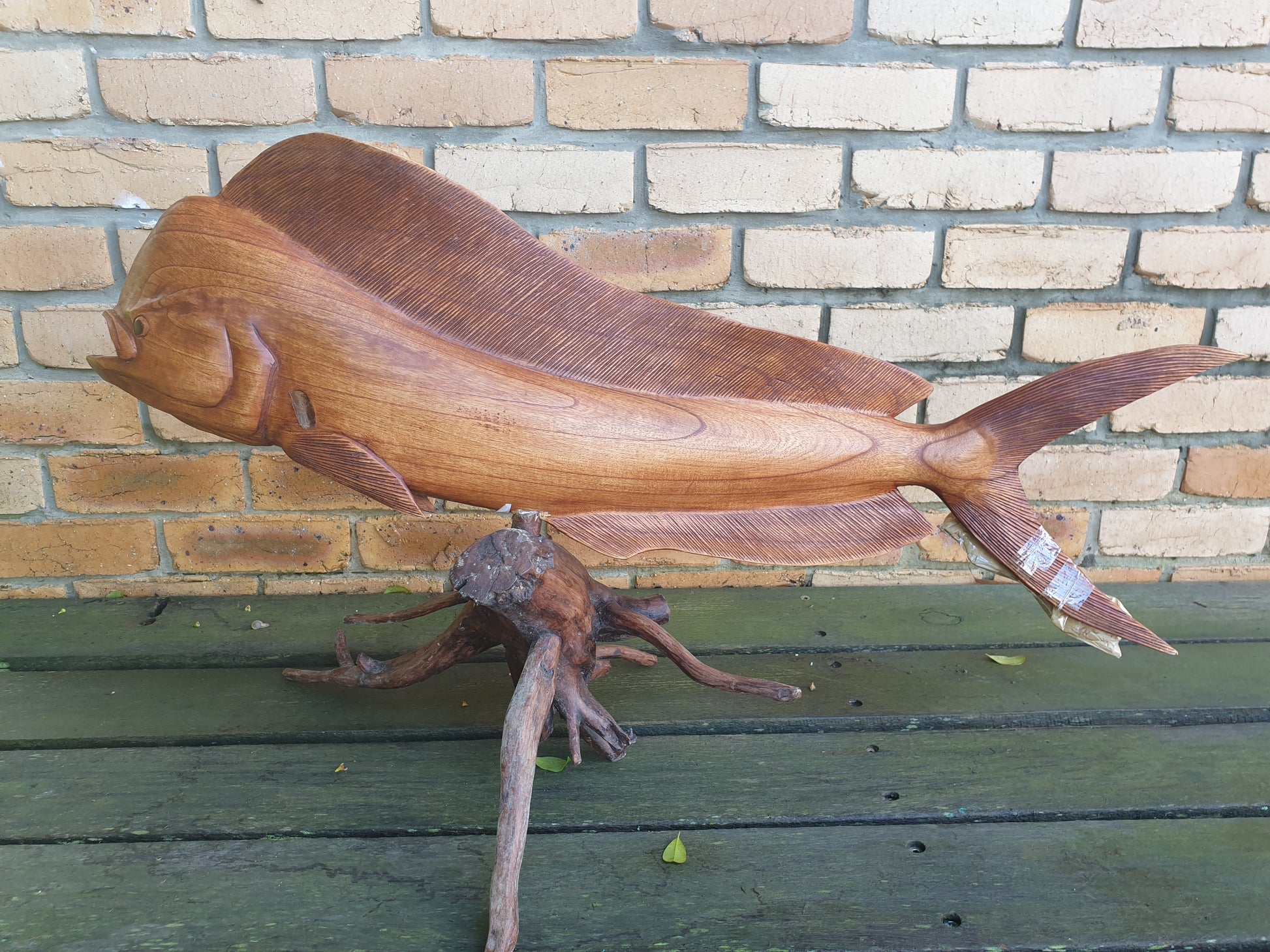 Wooden fish sculpture on a wooden surface with a brick wall background