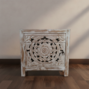 Close-up front view of a Mandala hand-carved Balinese bedside table in distressed whitewash finish on dark timber flooring with warm natural light casting shadows on the wall