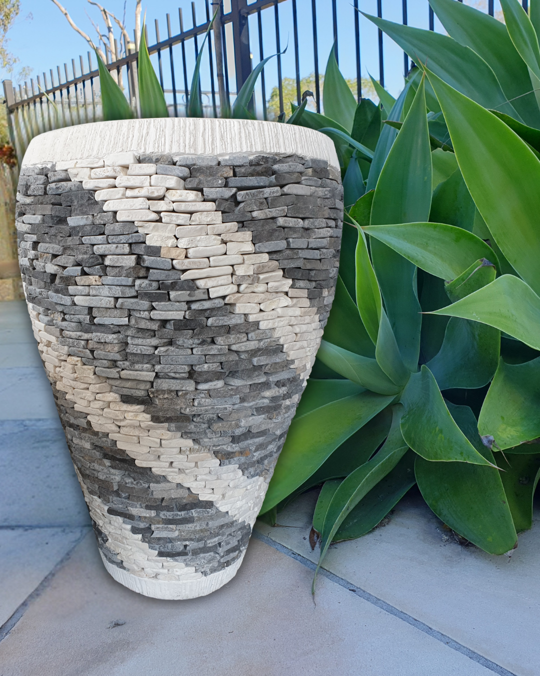 Decorative stone-patterned vase with green plants in the background