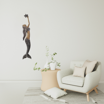 Decorative mermaid wall art above a modern armchair with a small table and plant in a minimalistic room.
