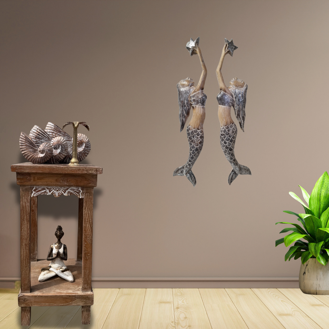 Decorative wall art carvings of mermaids on a beige wall with a wooden table and plant in the foreground.