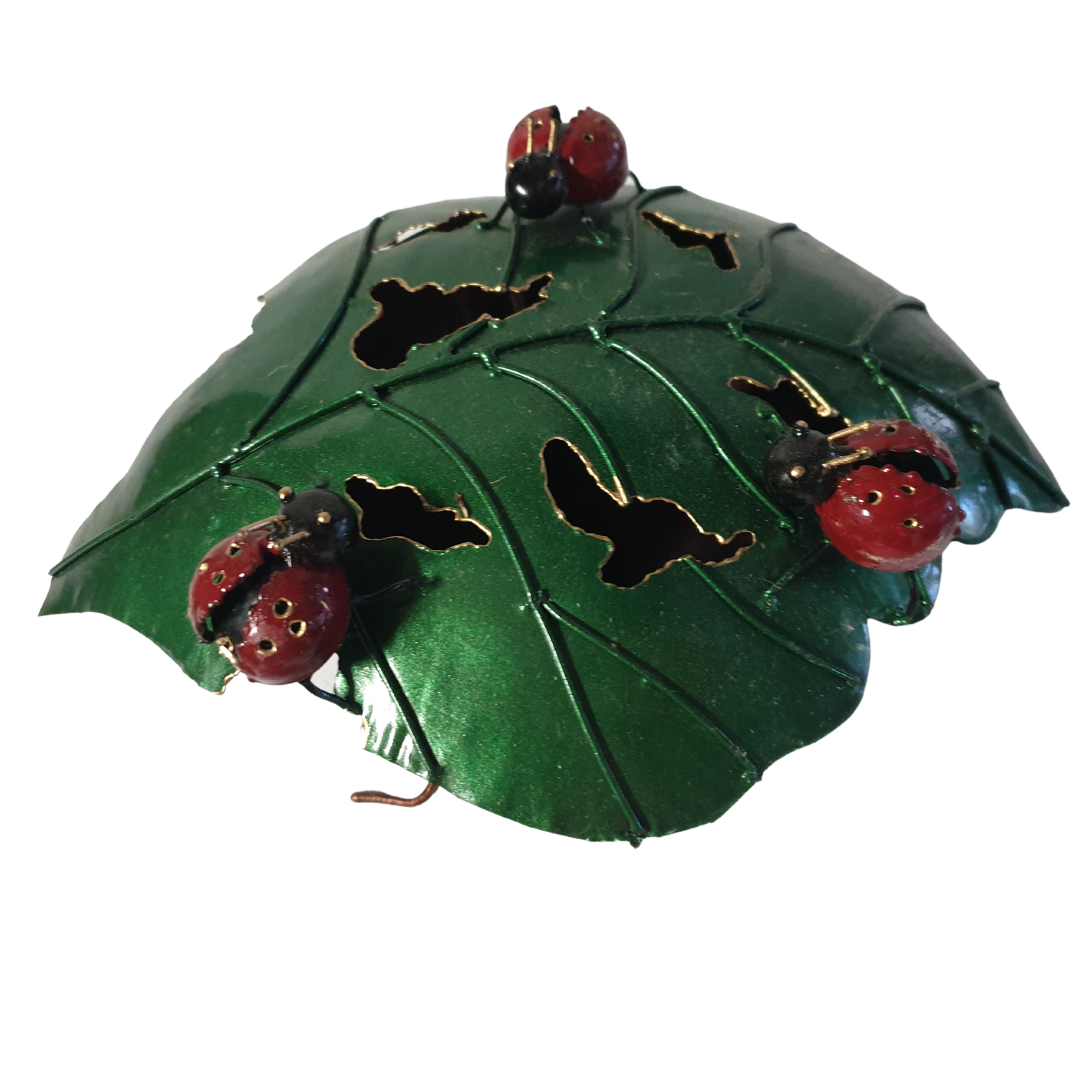 Decorative green leaf with cut-out shapes and ladybug designs on a white background
