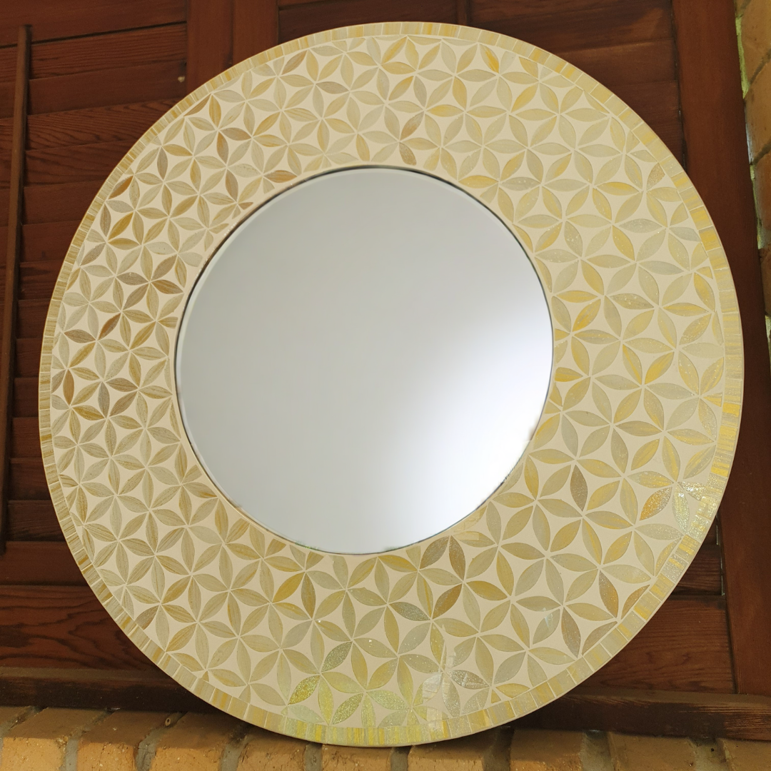 Round mirror with a decorative yellow and beige patterned frame on a wooden background
