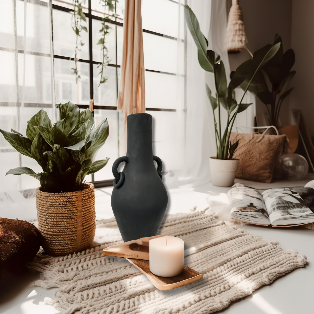 Decorative setting with plants, vase, candle, and books on a table by a window.