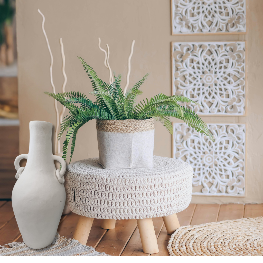 Decorative setting with a plant, vase, and woven stool against a textured wall.