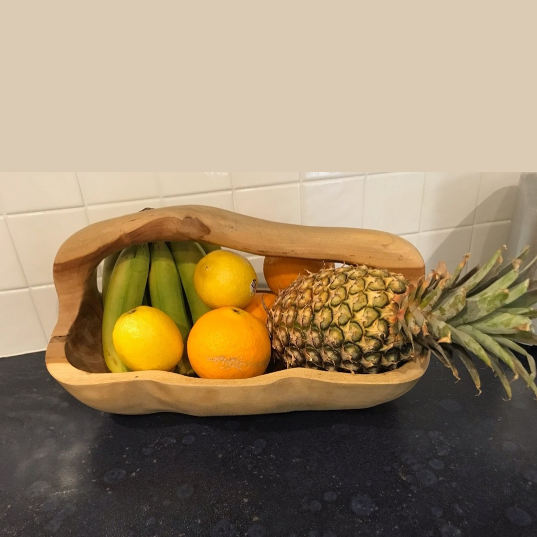 Wooden fruit basket with bananas, oranges, and a pineapple on a kitchen counter.