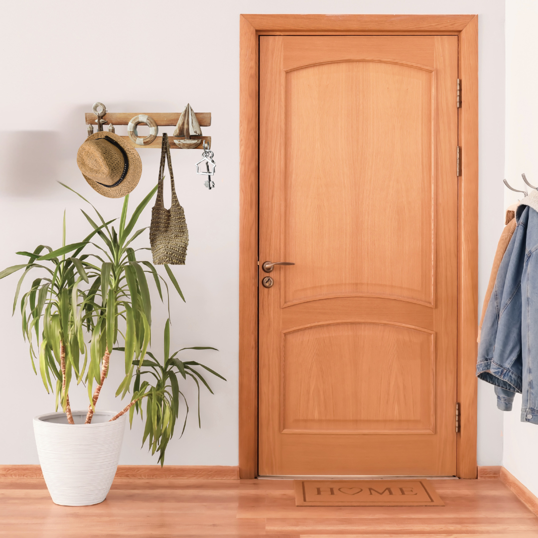 Wooden door with a plant, coat rack, and doormat on a wooden floor.