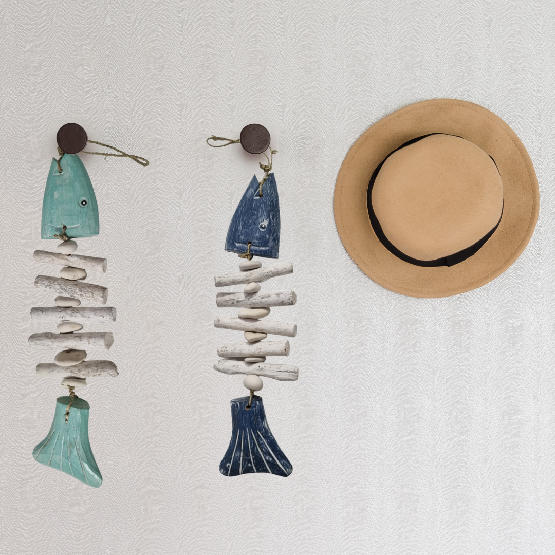 Two decorative fish ornaments made from driftwood and ceramic on a white background, with a straw hat beside them.