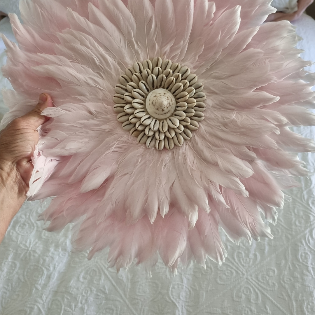 Pink feathered flower decoration held by a hand on a textured white surface