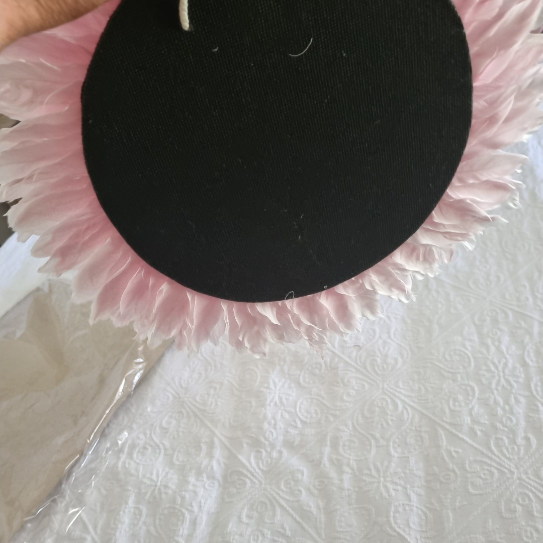 back of art Black circular object with pink fringe on a white textured surface