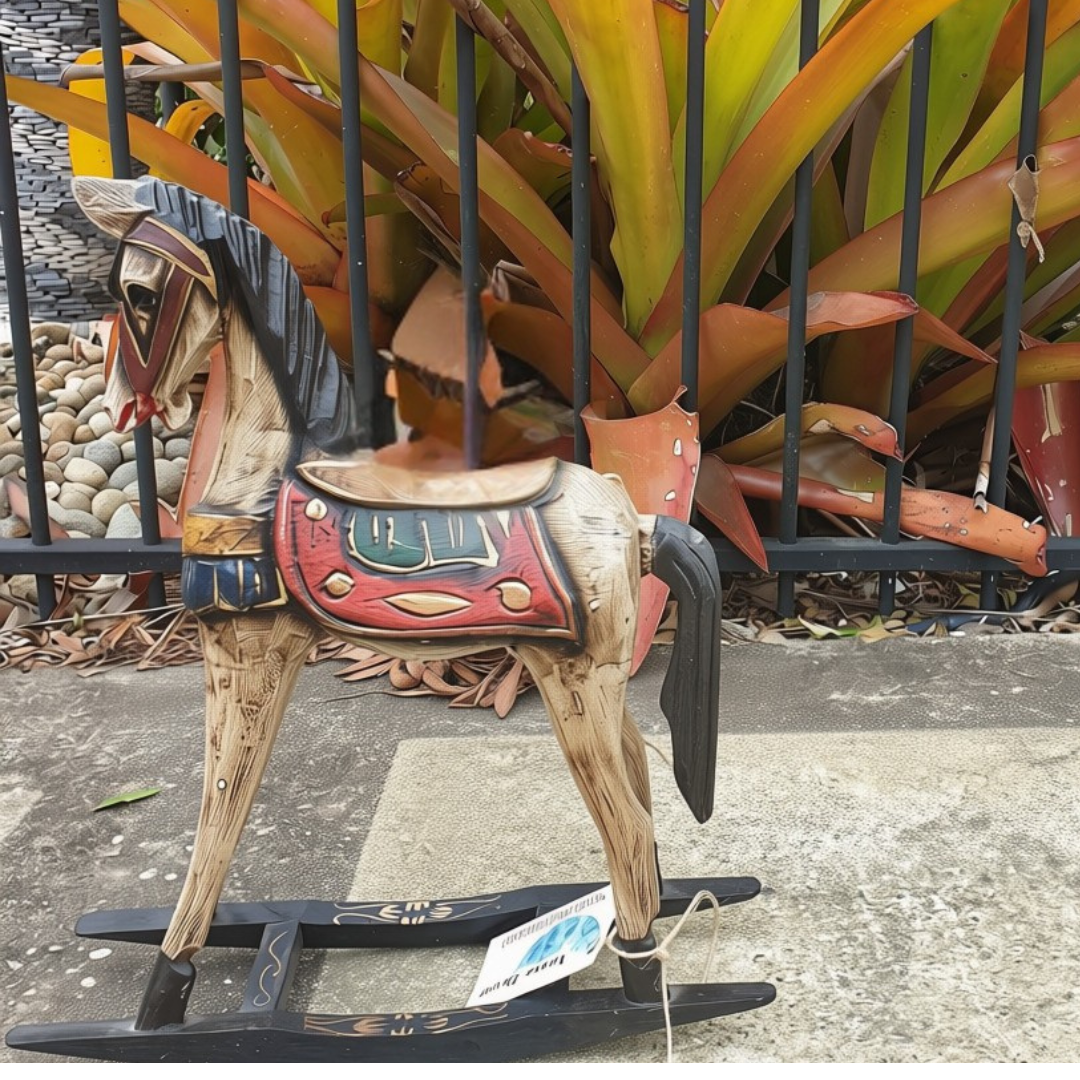 Painted rocking horse decorative feature with hand-carved red saddle and jewel tone detailing, photographed outdoors against tropical foliage