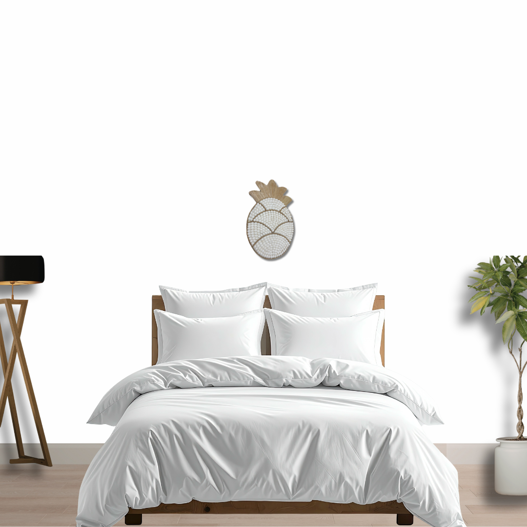 White bedding set on a bed with a decorative wall piece and plant in the background.