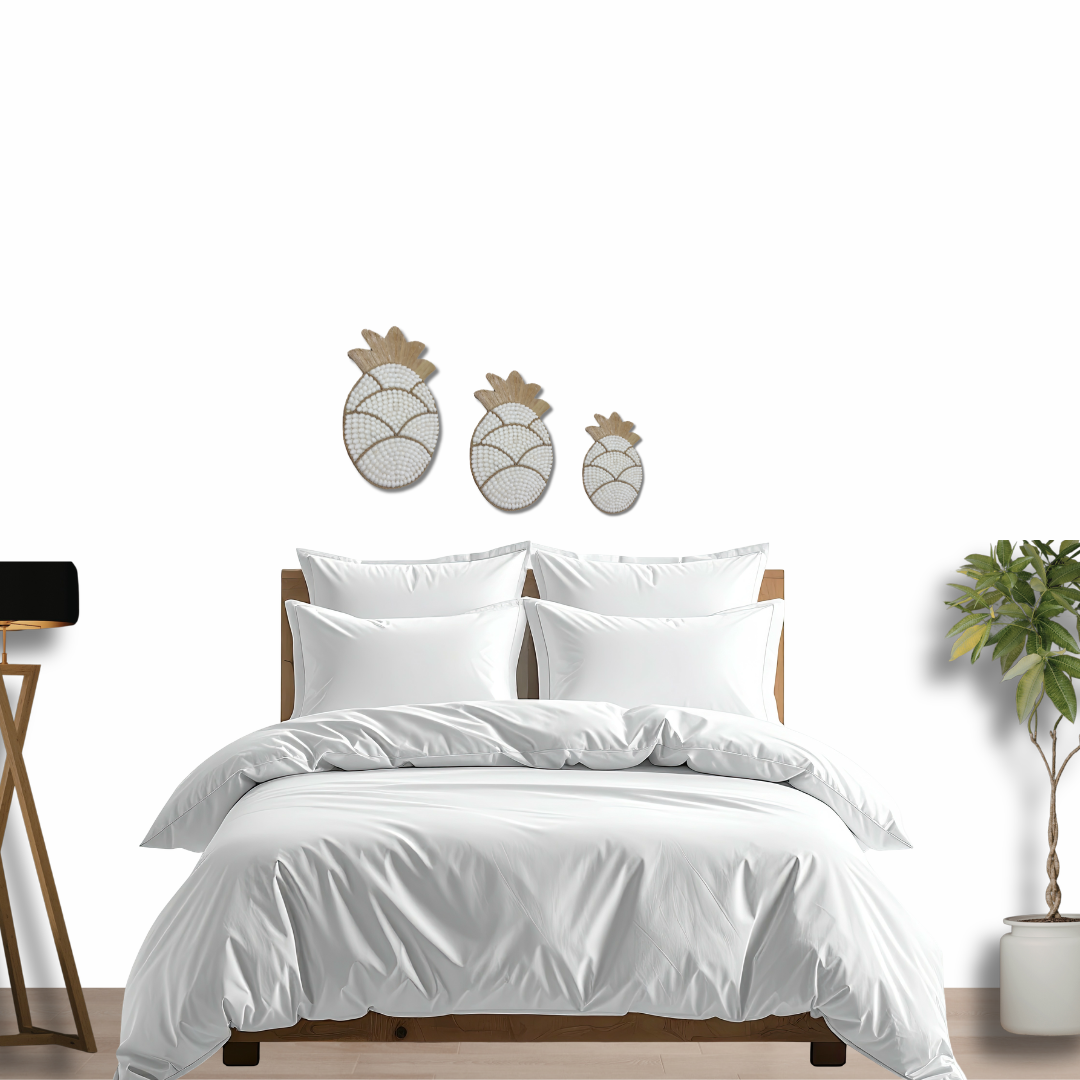 White bedding set on a bed with decorative Pineapple Shell Wall Art  and plant in the background