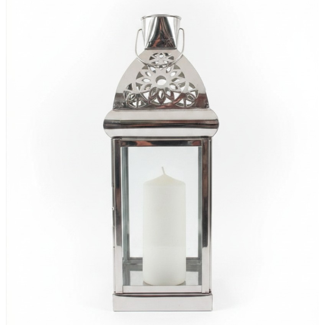 Medium polished silver metal lantern with ornate filigree-cut triangular roof, bucket handle, and single white pillar candle, photographed on a white background