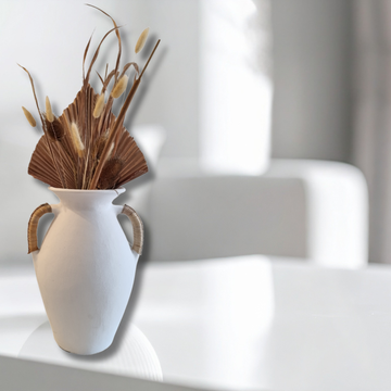 White vase with dried plants on a white surface
