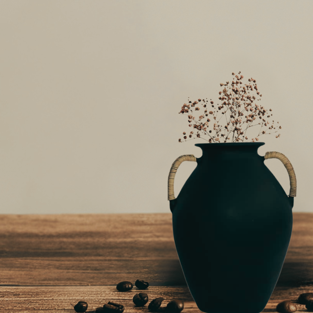 Black green vase with handles on a wooden surface, containing dried flowers, with coffee beans around.
