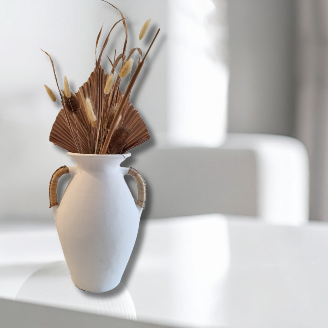 White vase with handles holding dried plants on a white surface