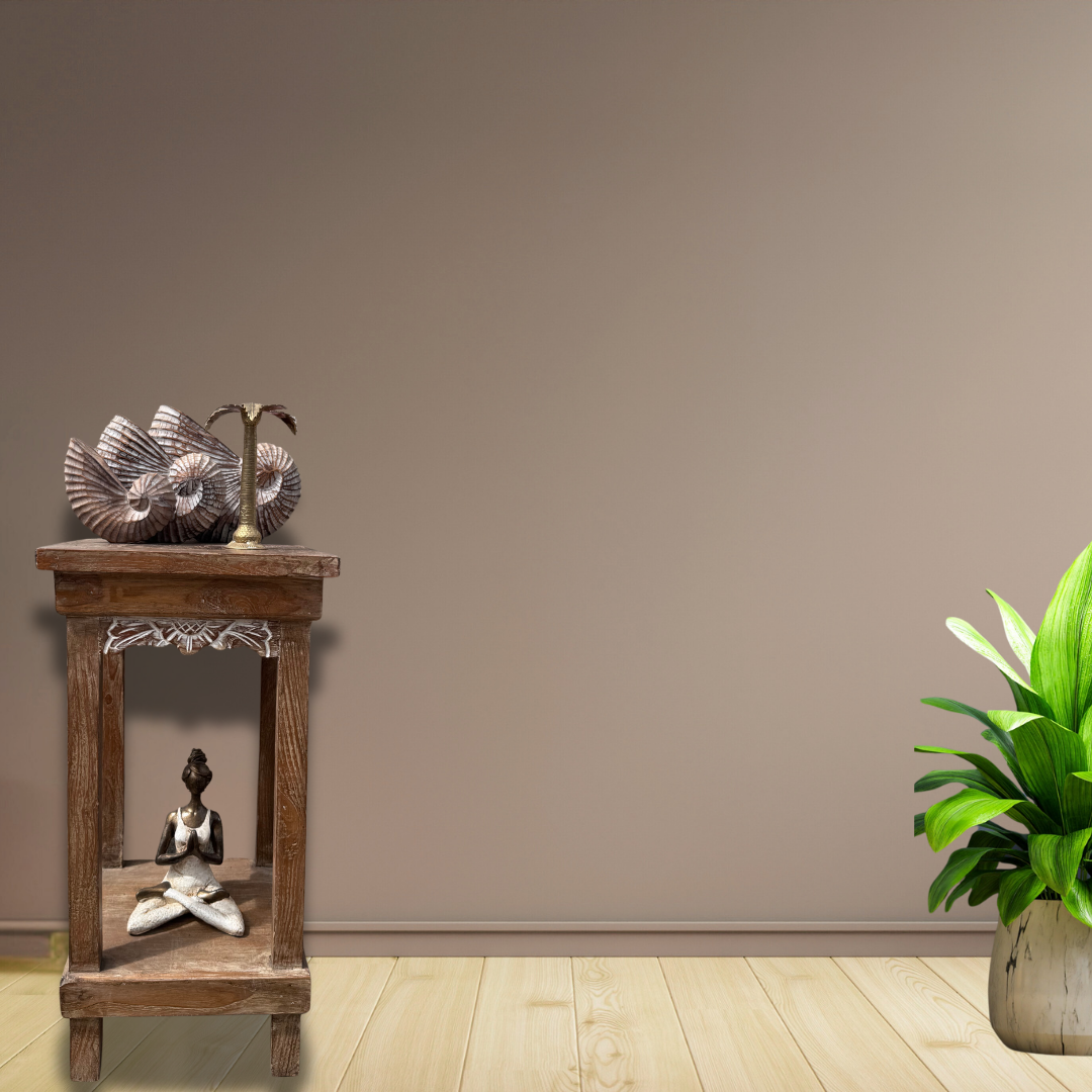 Wooden side table with decorative items against a plain wall with a plant on the right.