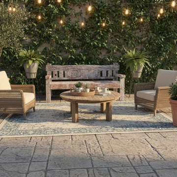 Reclaimed timber day bed furniture styled on a stone patio with wicker armchairs, round timber coffee table, string lights and lush greenery