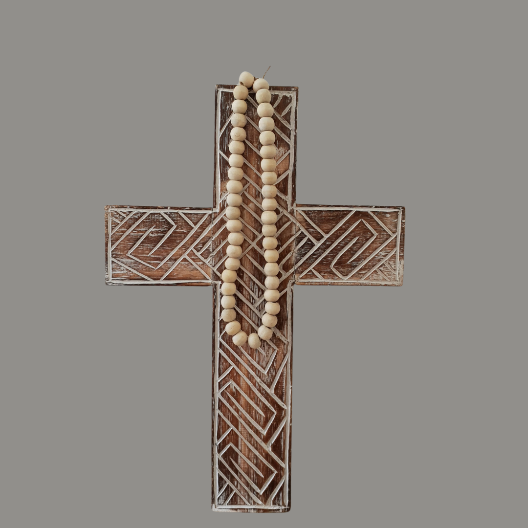 Wooden cross with geometric patterns and a string of beads on a gray background