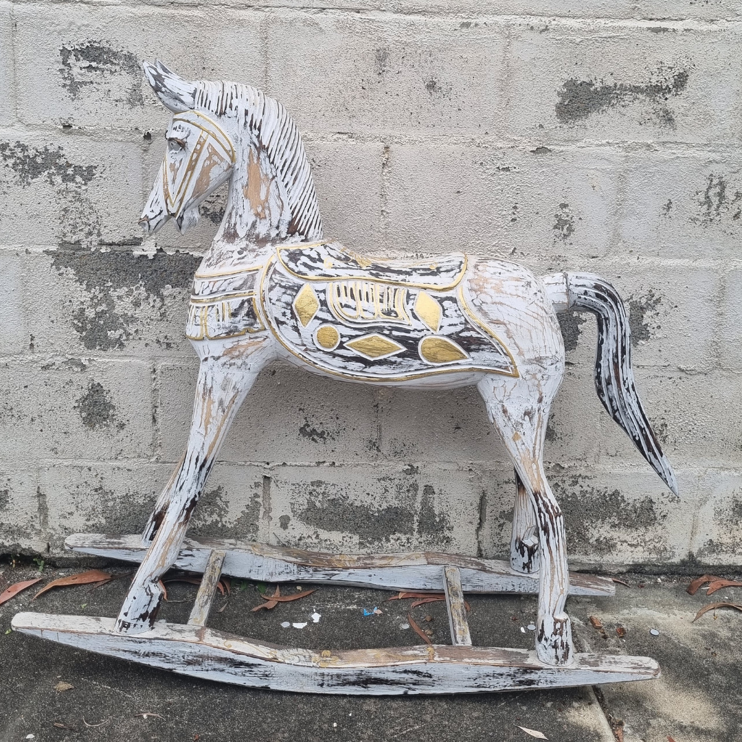 Front-facing view of a large hand-carved with crackled whitewash finish and gold geometric saddle detailing, photographed against a concrete block wall outdoors