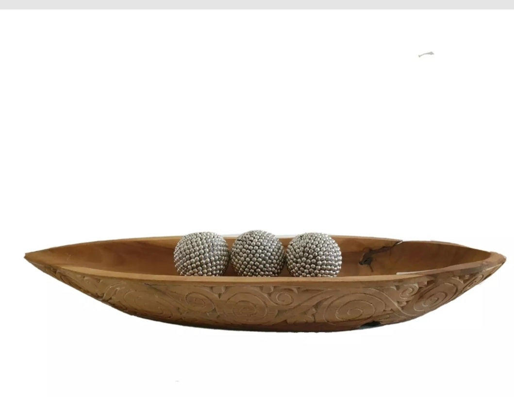 Carved teak wood boat tray with three silver decorative spheres resting inside, on a white surface