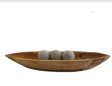 Carved teak wood boat tray with three silver decorative spheres resting inside, on a white surface