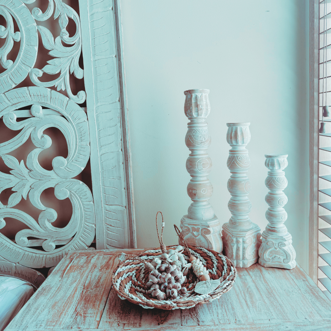 Decorative white candlesticks and a woven basket on a wooden surface with a decorative mirror in the background.