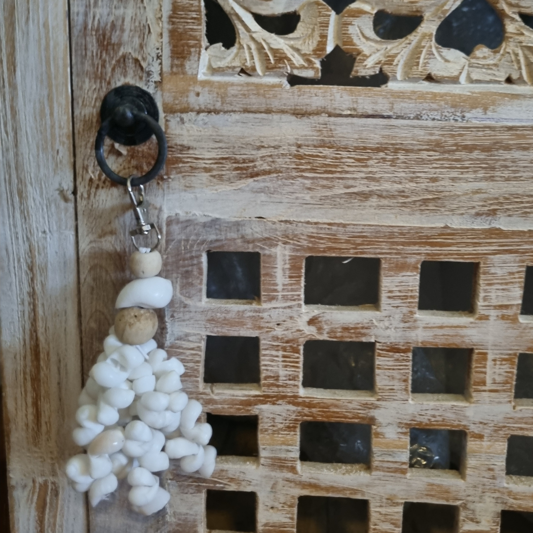 Coastal shell tassel with wooden beads hanging from a black iron ring on a carved whitewashed timber door