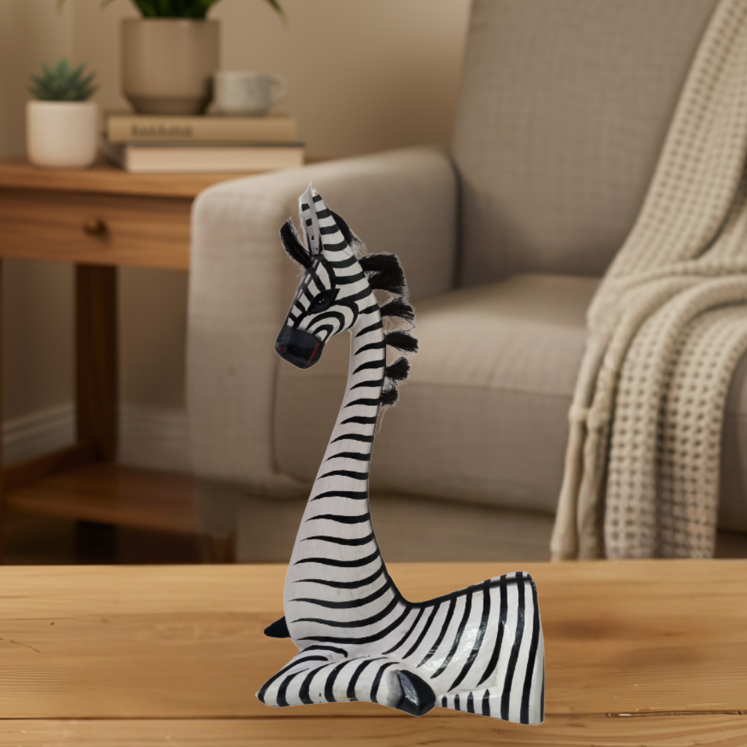 Sitting Zebra Statues Wooden Designs Medium white and black striped wooden  figurine on a timber table with a grey armchair in the background

