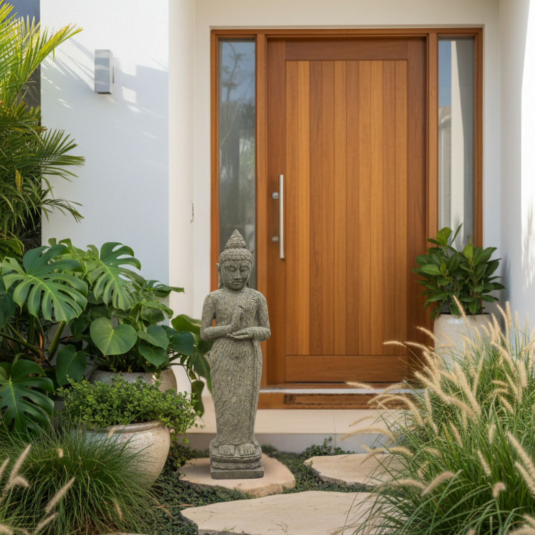 Dark olive-grey stone garden statue styled beside a modern coastal home entry with a timber door, monstera, ornamental grasses and stepping stones