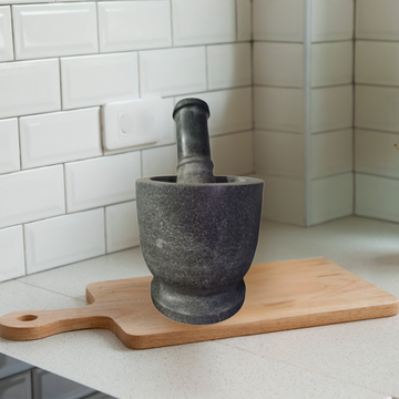 Mortar and pestle on a wooden cutting board against a tiled kitchen wall.