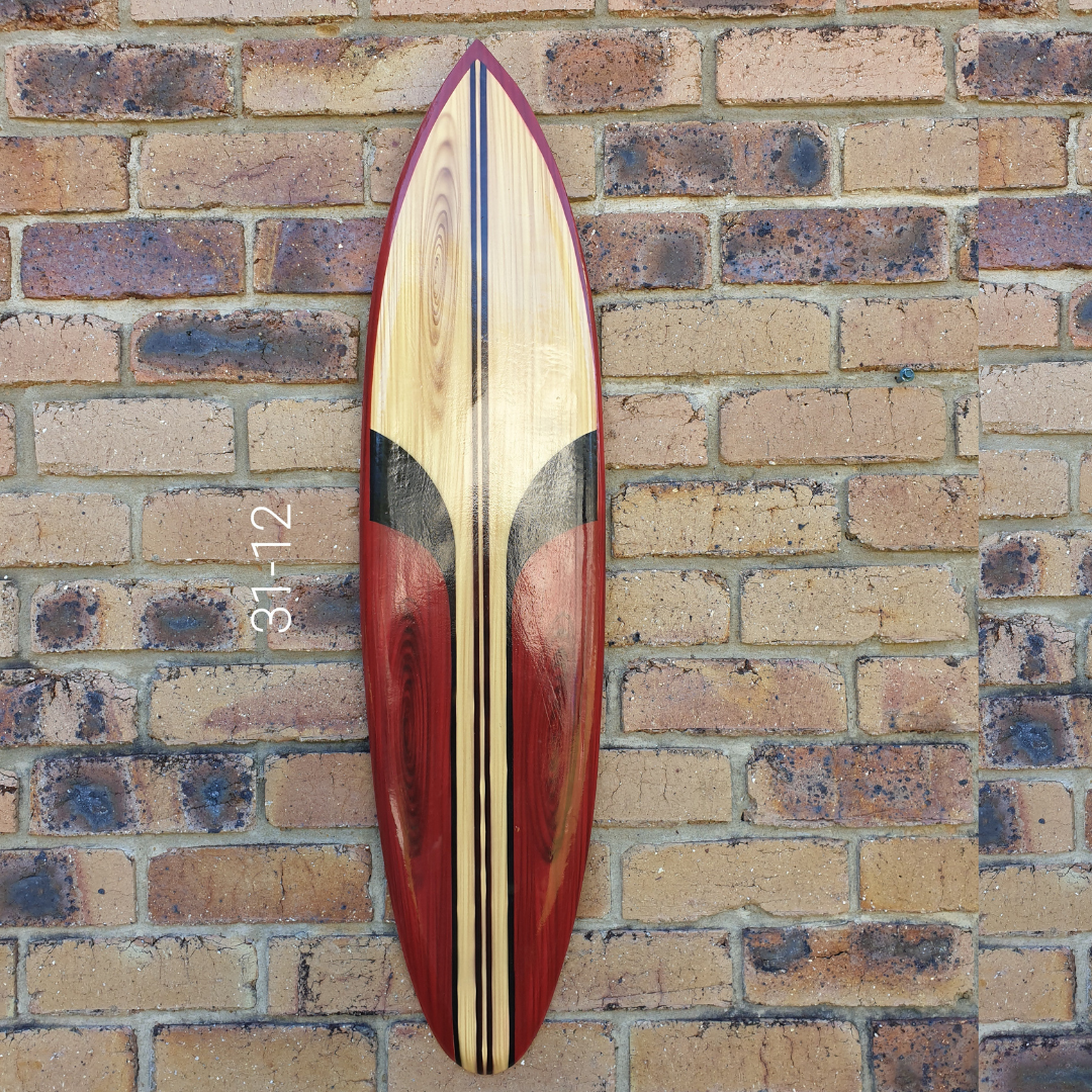 Wooden surfboard with red and black design on a brick wall