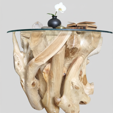 Teak root coffee table with round glass top styled with a black ceramic vase with white orchid, stacked books, and crystal quartz on the glass surface against a soft grey background